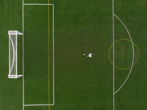 Overhead view of soccer field with player standing in front of the penalty box.