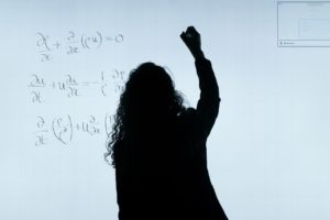 A woman writing math problems on a board representing a person teaching classes at night as an independent contractor.